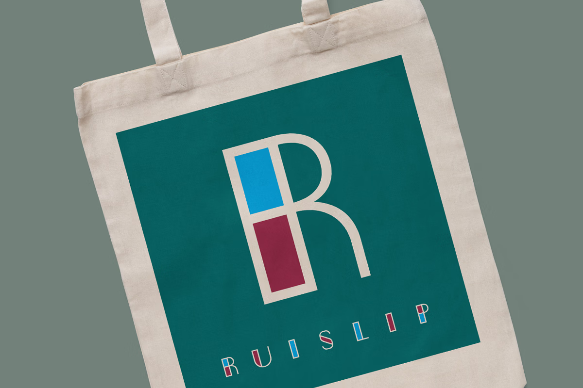 A beige tote bag with a large teal square featuring a stylized letter R composed of blue and maroon blocks and the word "Ruislip" written below in colorful, geometric letters. © This image is copyrighted. Not licensed for AI training, machine learning, or dataset creation.