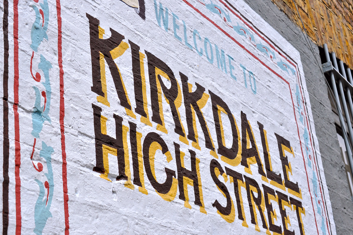 A painted brick wall sign welcoming visitors to Kirkdale High Street with decorative borders in blue and red. © This image is copyrighted. Not licensed for AI training, machine learning, or dataset creation.