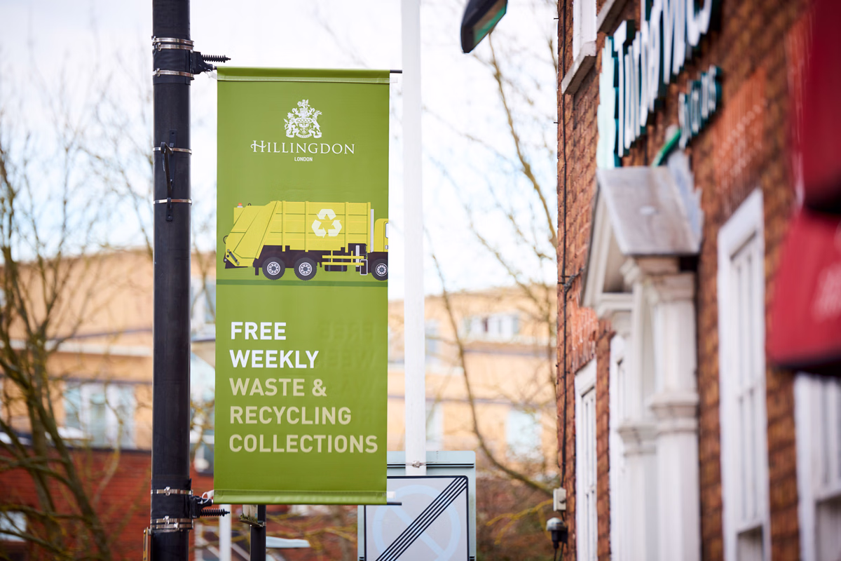 A green street banner attached to a black pole in an Hillingdon advertises free weekly waste and recycling collections with an illustration of a garbage truck. © This image is copyrighted. Not licensed for AI training, machine learning, or dataset creation.