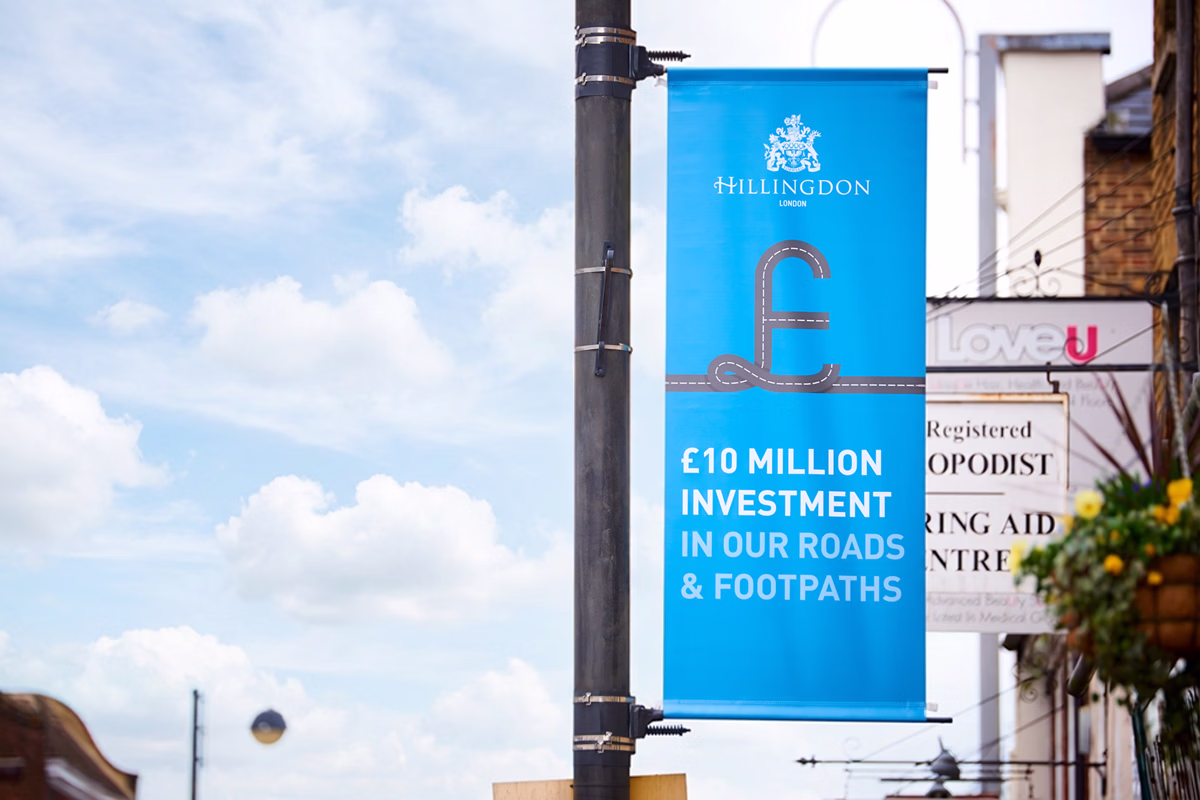 A blue street banner attached to a pole that displays the message"ten million pound investment in roads and footpaths" with a sky in the background. © This image is copyrighted. Not licensed for AI training, machine learning, or dataset creation.