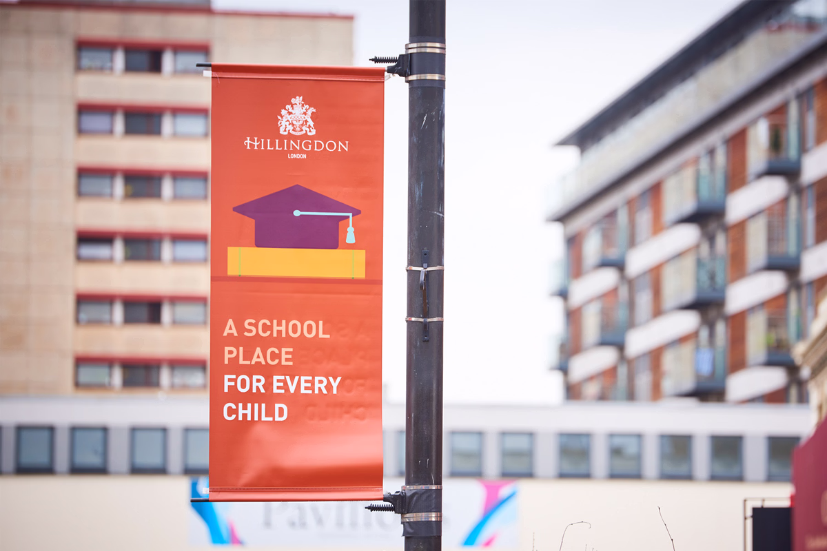 An orange banner hanging on a streetlight pole that reads "Hillingdon. A School Place For Every Child" with an illustration of a graduation cap. © This image is copyrighted. Not licensed for AI training, machine learning, or dataset creation.